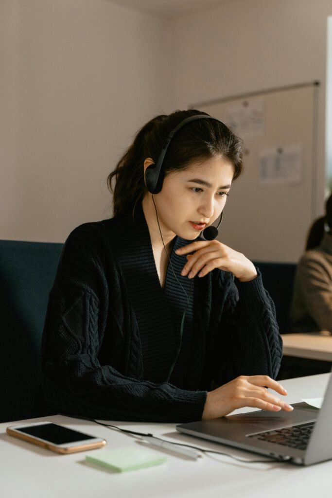 Focused female customer support agent in an office using a laptop and headset.